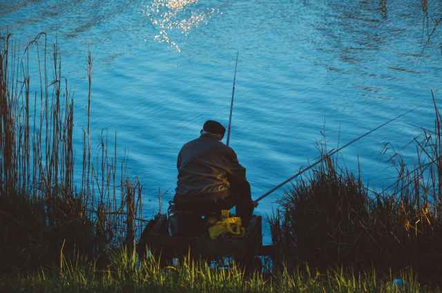 man sitting on the chair while doing fishing near body of water