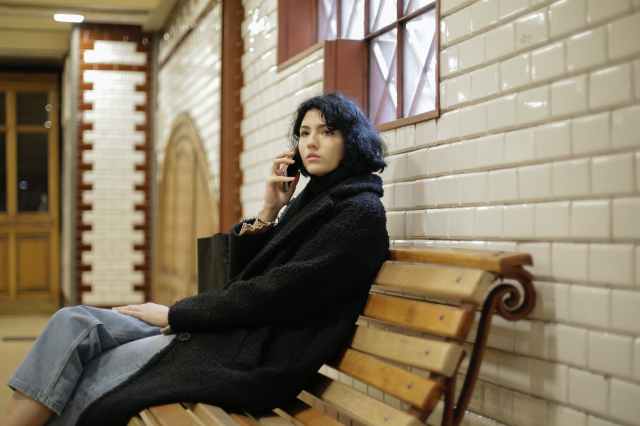woman in black coat sitting on brown wooden bench