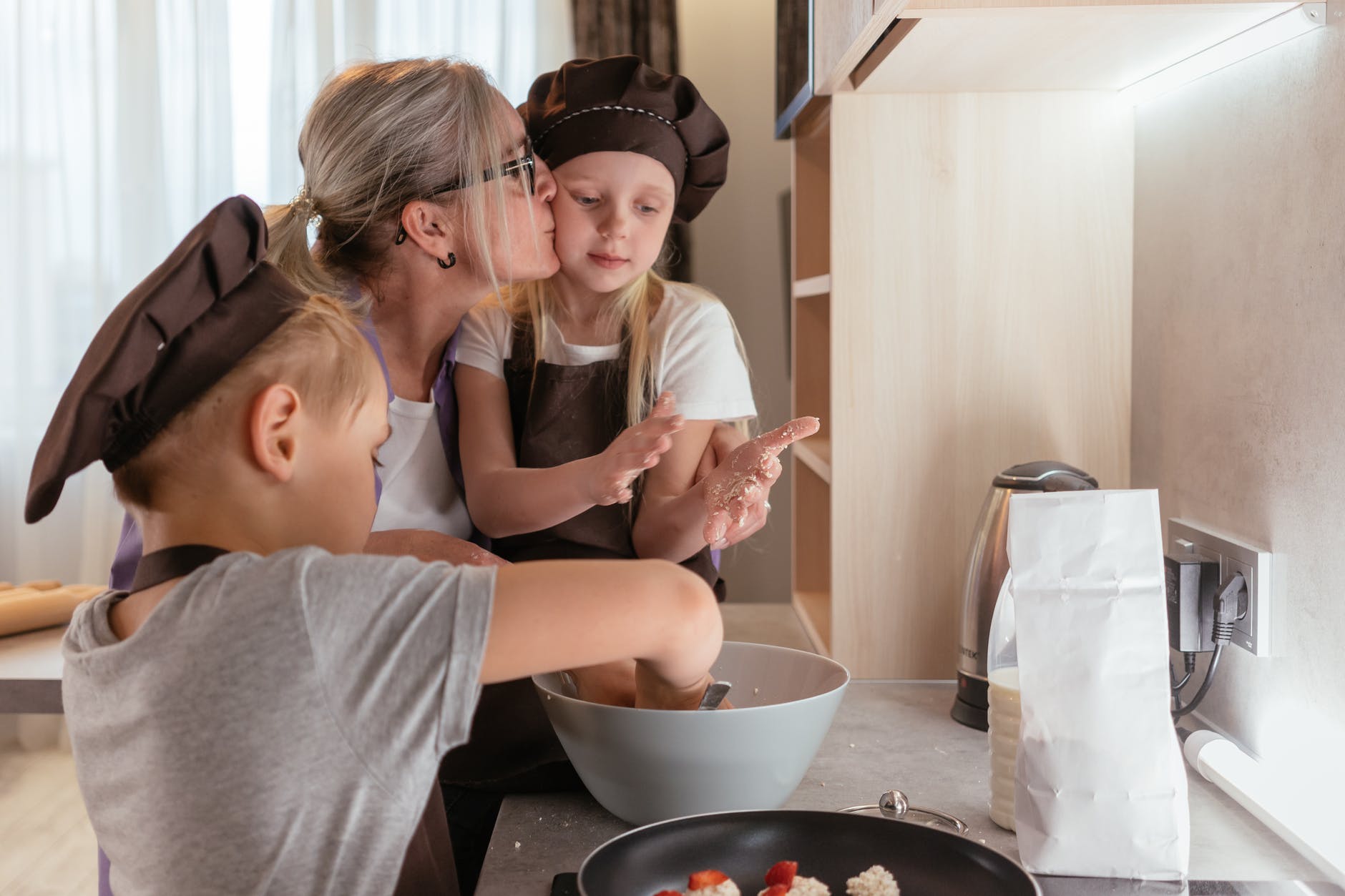 elderly woman kissing granddaughter in her cheek while cooking