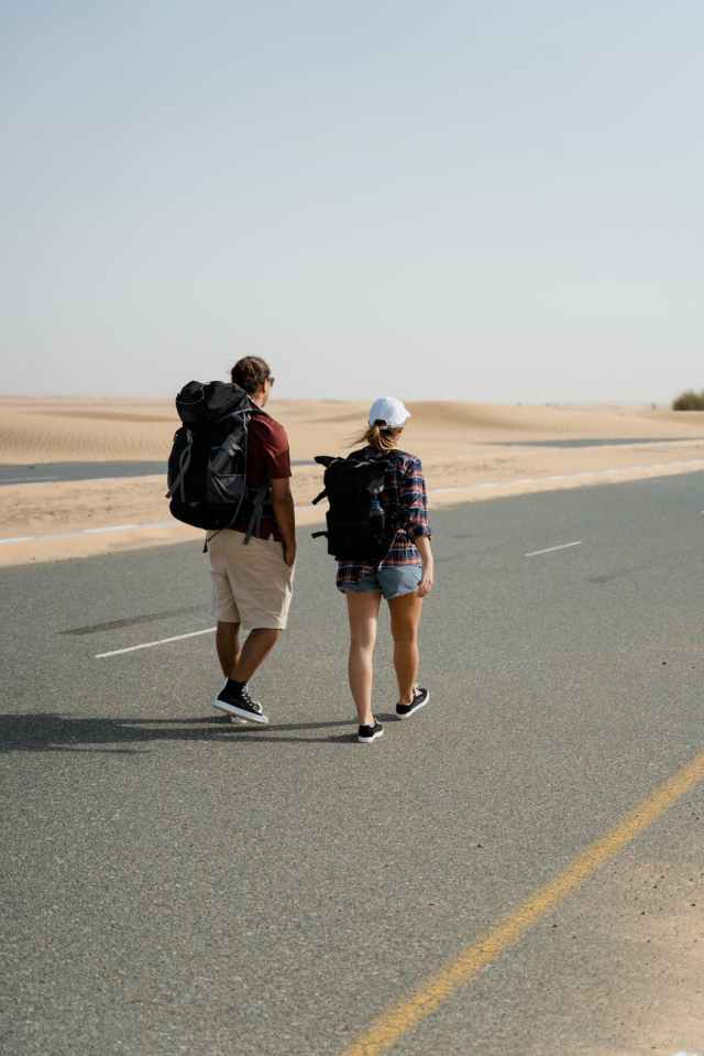 man and woman walking on the road while carrying their rucksack bag