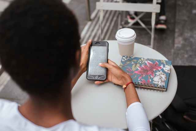 unrecognizable black woman messaging on phone at cafe